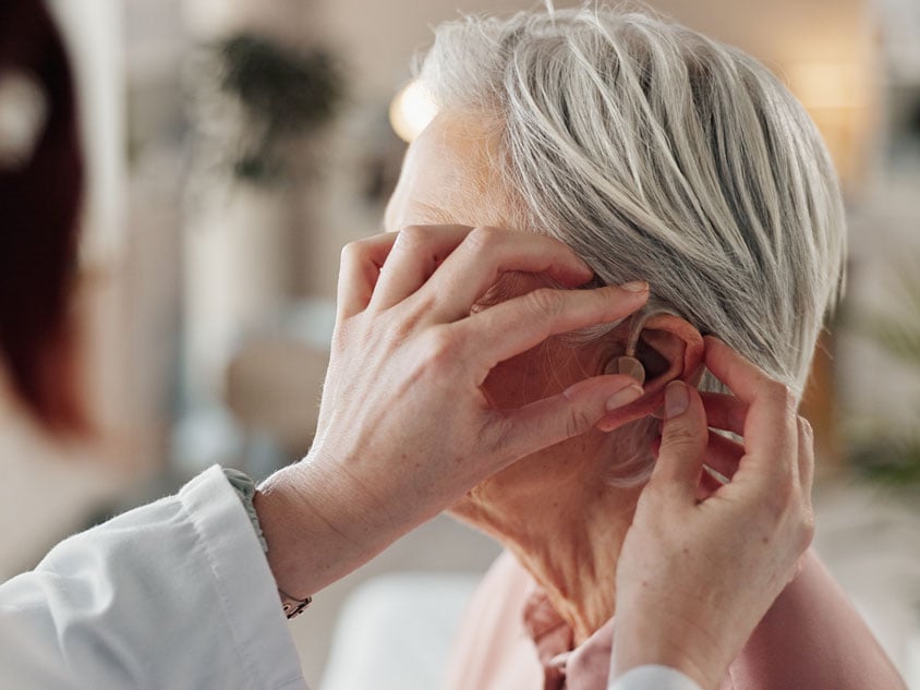 A hearing aid is fitted to a woman's ear