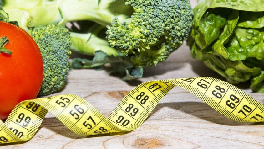Measuring tape in front of broccoli and a tomatoe